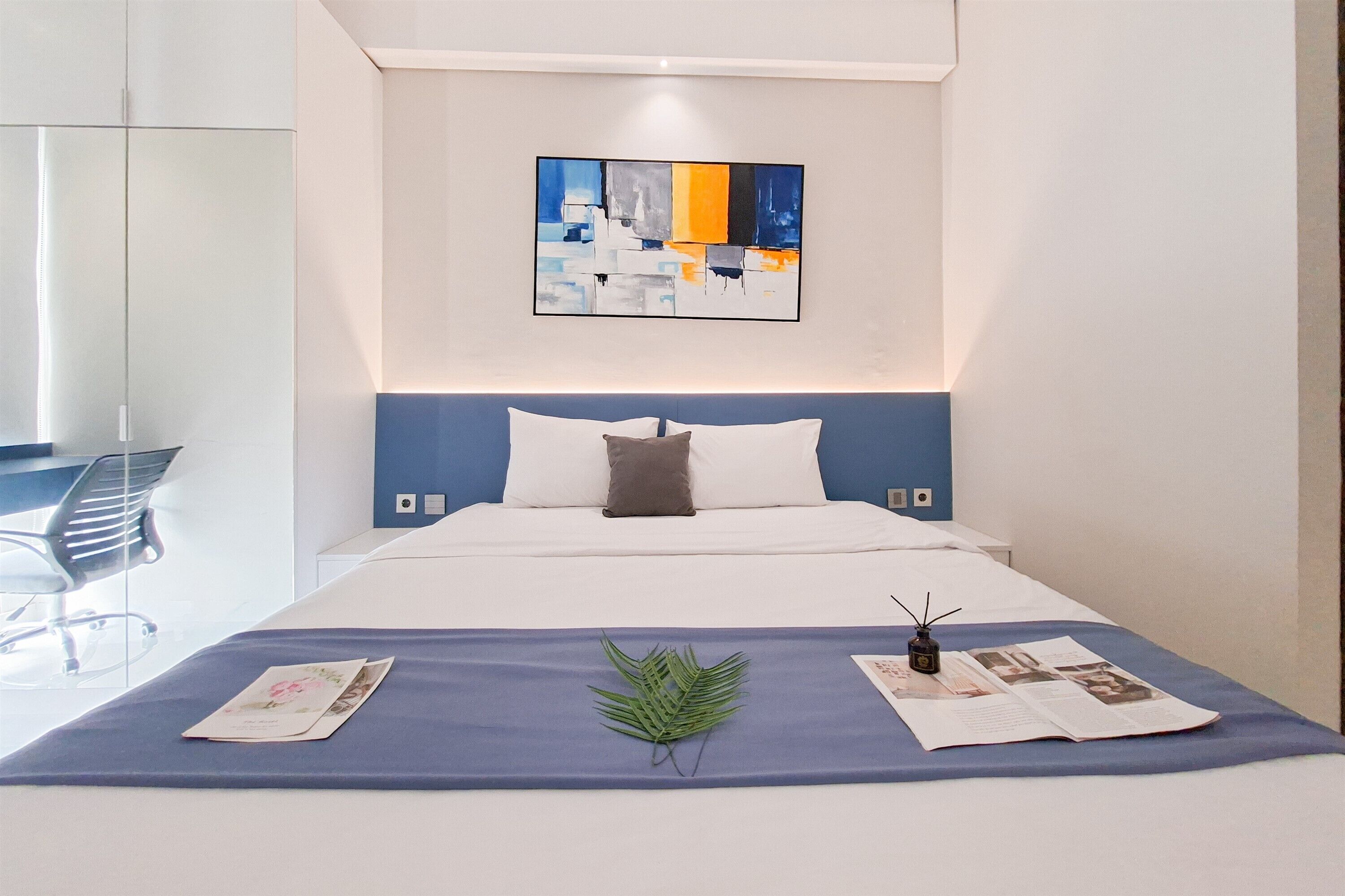 Een moderne hotelkamer met een net opgemaakt bed, een blauwe accentmuur en een eigentijds abstract schilderij erboven.
