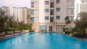 A swimming pool with lounge chairs and a lifebuoy, surrounded by greenery and tall residential buildings. - Scandinavian Modern Studio Apartment At Springhill Terrace Residence (Jakarta)