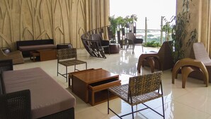 A modern lounge with a high ceiling, a large window offering a view, and a variety of seating options including sofas, chairs, and a unique curved chair. - Scandinavian Modern Studio Apartment At Springhill Terrace Residence (Jakarta)