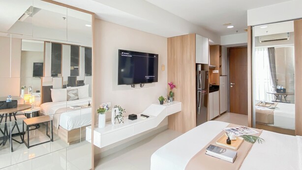 A modern hotel room with a bed, bedside table, TV, and a kitchenette. - Scandinavian Modern Studio Apartment At Springhill Terrace Residence (Jakarta)