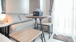 A modern hotel room with a sofa, two small tables, a lamp, and a travel kit on the sofa. - Scandinavian Modern Studio Apartment At Springhill Terrace Residence (Jakarta)
