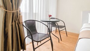 A room with a bed, two wicker chairs, a small round table with a potted plant, and sheer curtains. - Studio Near Rajawali Station At Amethyst Apartment (Jakarta)