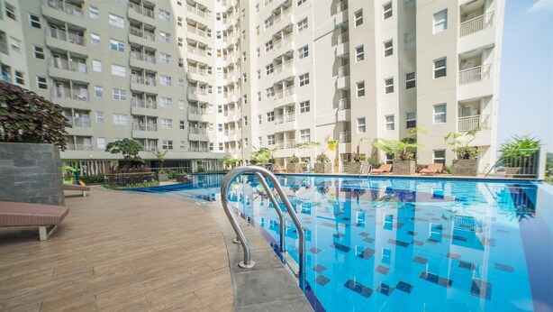 An indoor swimming pool with tiled flooring, metal railings, and a backdrop of multi-story residential buildings. - 1Br Near Unpar At Parahyangan Residence Apartment (Bandung)
