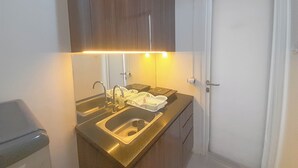 A compact kitchen with a double sink, a stove, and a cabinet above the counter. - 1Br Near Unpar At Parahyangan Residence Apartment (Bandung)