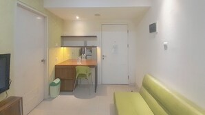 A compact room with a kitchenette, a small dining table with chairs, a bench, and a trash bin. - 1Br Near Unpar At Parahyangan Residence Apartment (Bandung)
