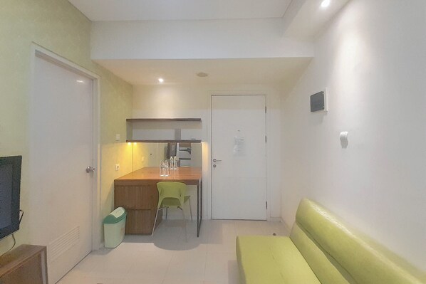 A compact room with a kitchenette, a small dining table with chairs, a bench, and a trash bin.
