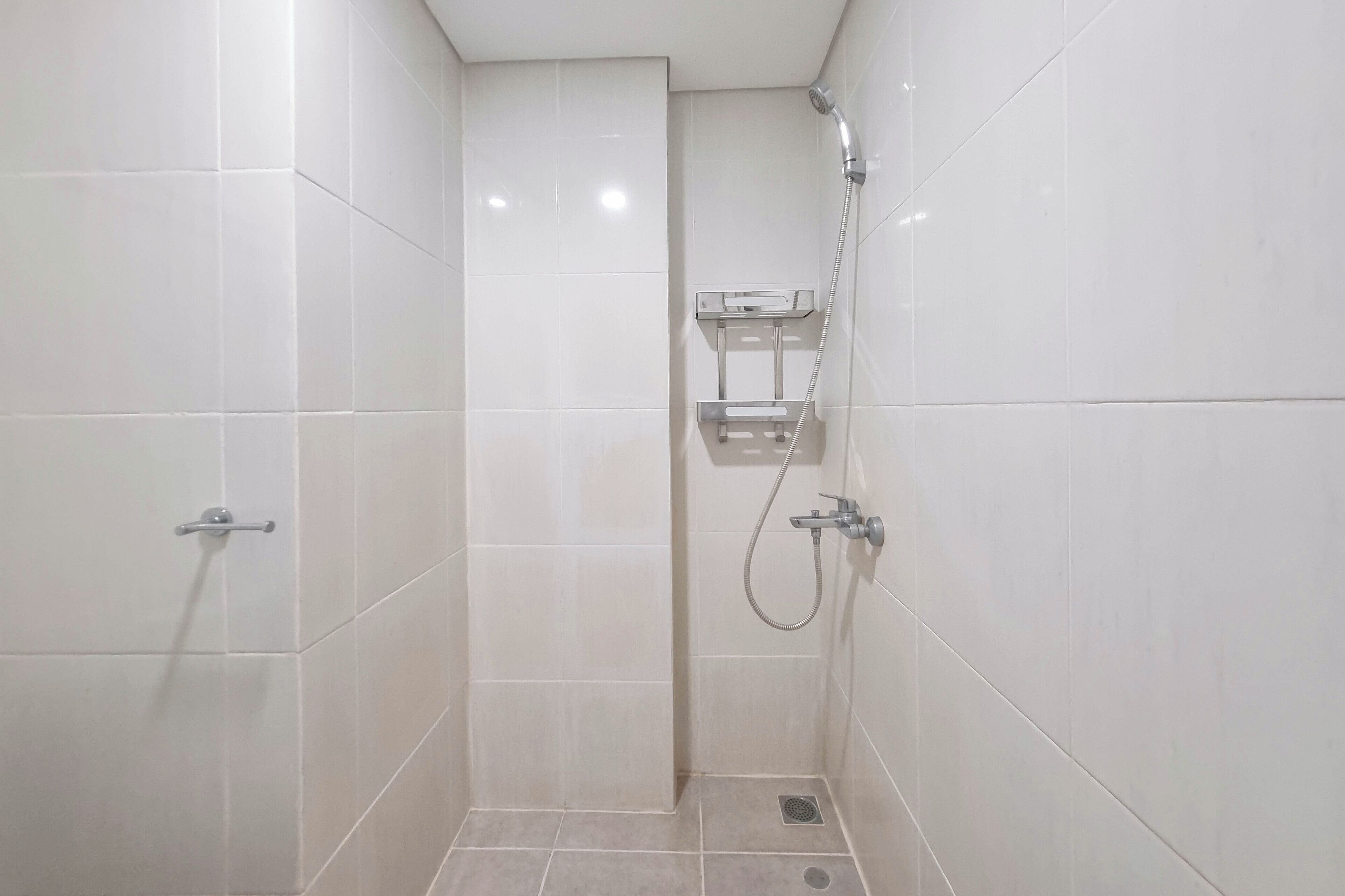 Un pequeño espacio de ducha con azulejos, un cabezal de ducha manual y un grifo instalado en la pared.