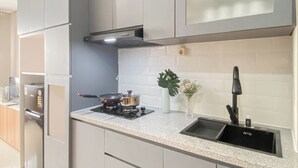 A modern kitchen with grey cabinets, a stainless steel range hood, a gas stove, a sink, and a vase with flowers. - Soft Grey 1Br At Royal Sentul Park Apartment (Bogor)