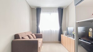 A modern living room with a sofa, a TV, and a refrigerator. - Soft Grey 1Br At Royal Sentul Park Apartment (Bogor)
