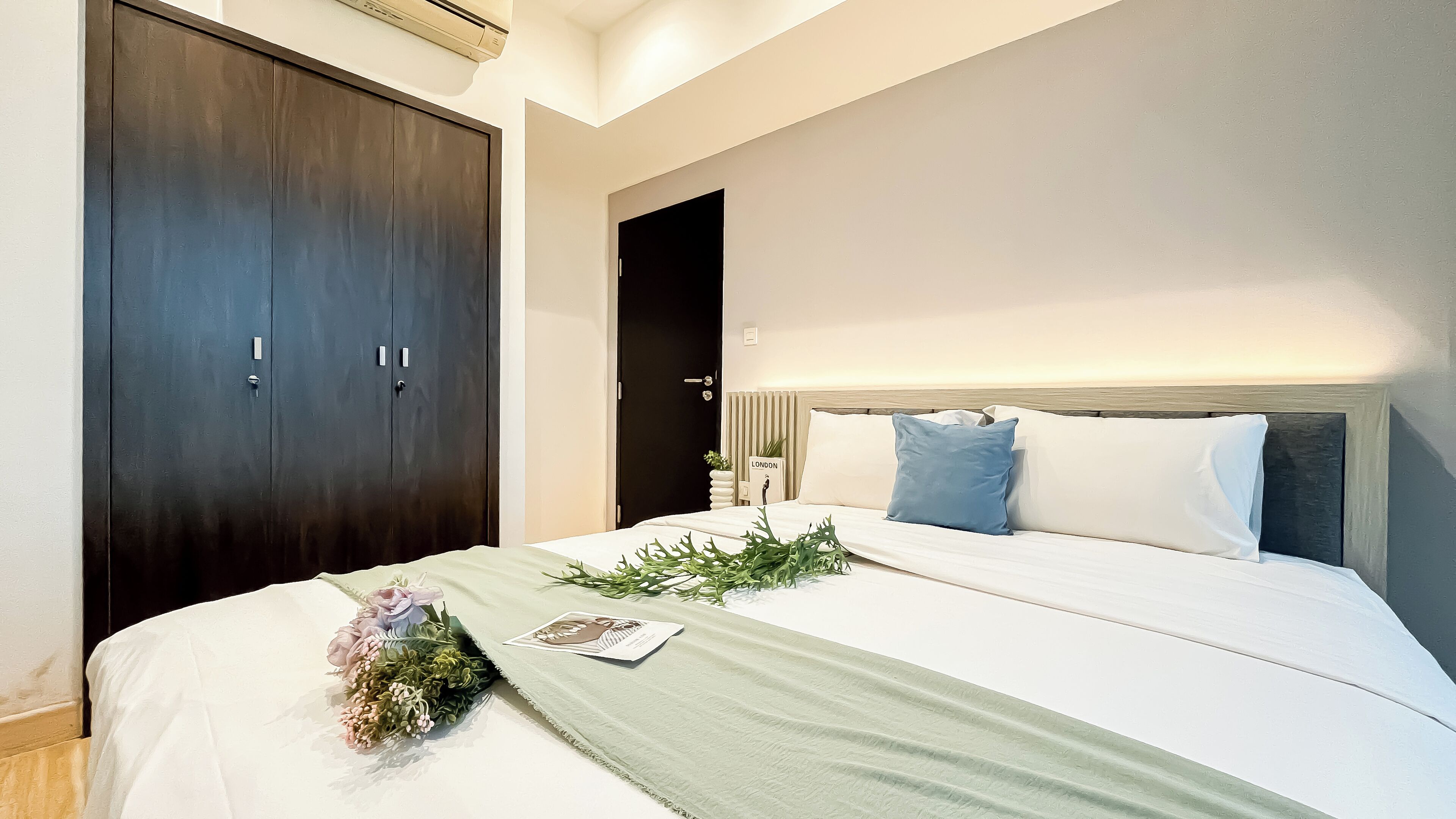 A bedroom with a bed, a dark wardrobe, a nightstand with a lamp, and a view of the sea.