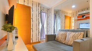 A modern living room with a sofa, a glass coffee table, a TV, and a wall-mounted air conditioning unit. - 2Br Near Mall At Cinere Bellevue Suites Apartment (Depok)