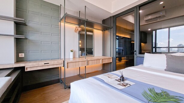 Habitación de hotel moderna con una cama grande, un escritorio con silla, una mesita con planta y un ventanal con vistas a la ciudad.