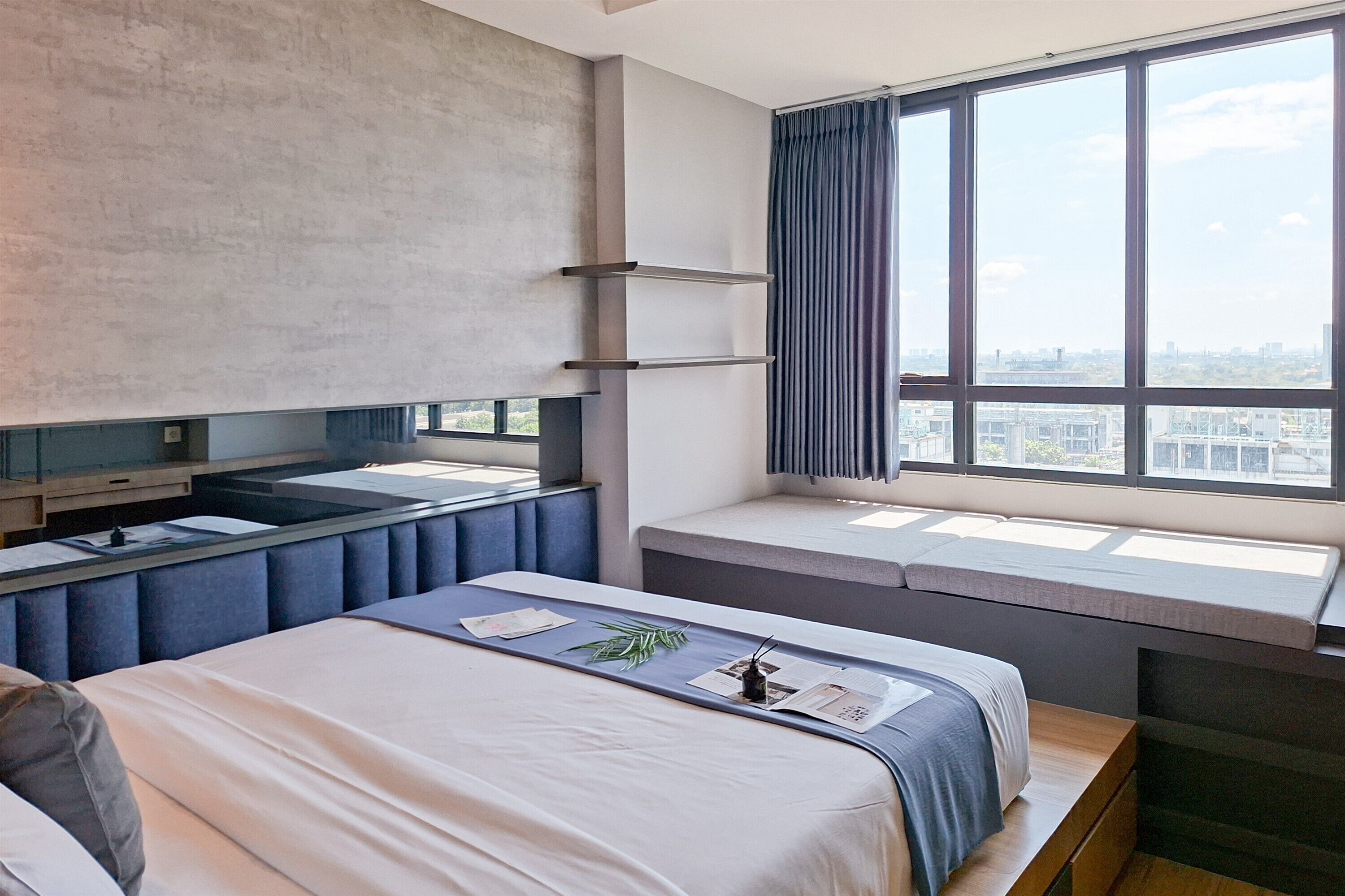 A modern hotel room with a large bed, a built-in desk, a window with a city view, and a large mirror.