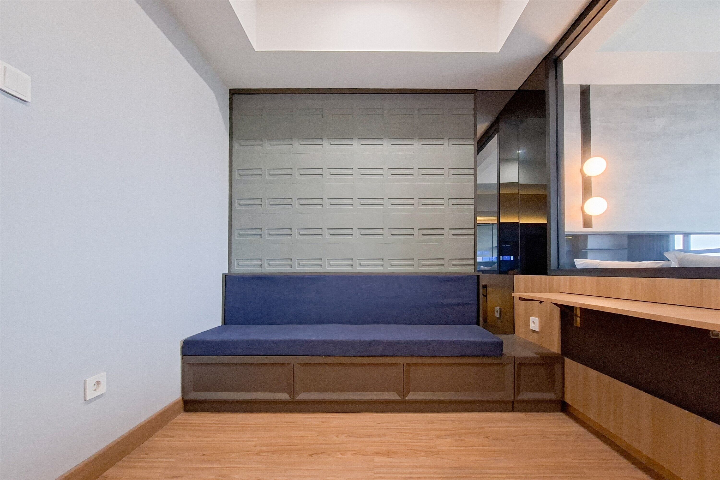 A compact room with a built-in bench, a wooden floor, a wall-mounted light fixture, and a large mirror.