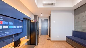Una sala de estar moderna con un televisor de pantalla plana, piso de madera, un sofá oscuro y una cocina al fondo.