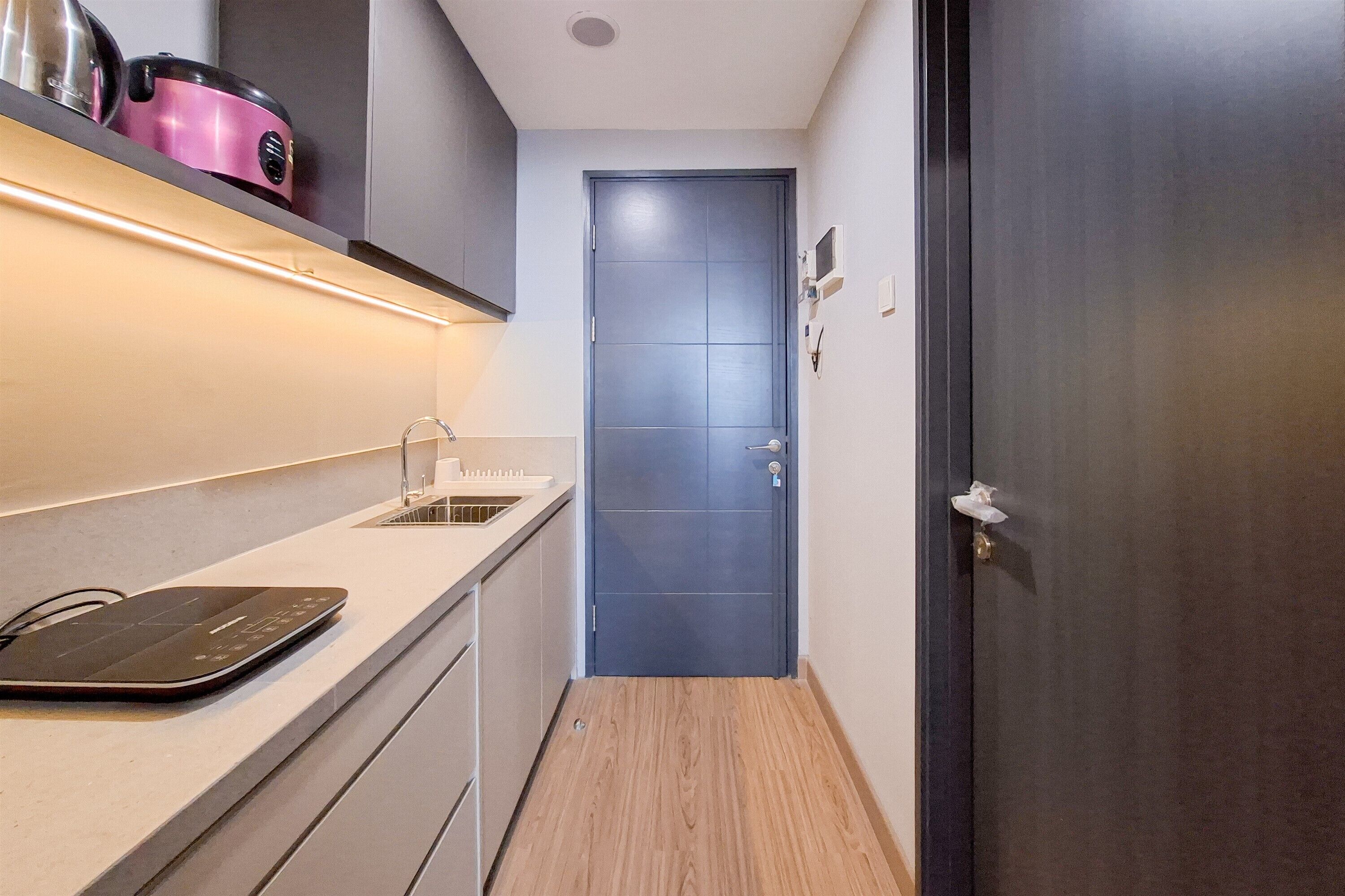 A narrow hallway with a wooden floor, a blue door, and a countertop with a kettle and a kettle warmer.