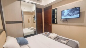 A hotel room with a bed, a television mounted on the wall, a mirror, and a wardrobe. - 2Br Near Marvell City Mall At Linden Apartment (Surabaya)