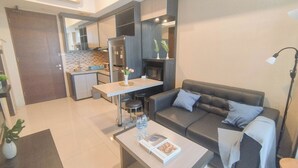 A modern living room with a sofa, coffee table, and a dining area with a kitchen in the background. - 2Br Near Marvell City Mall At Linden Apartment (Surabaya)