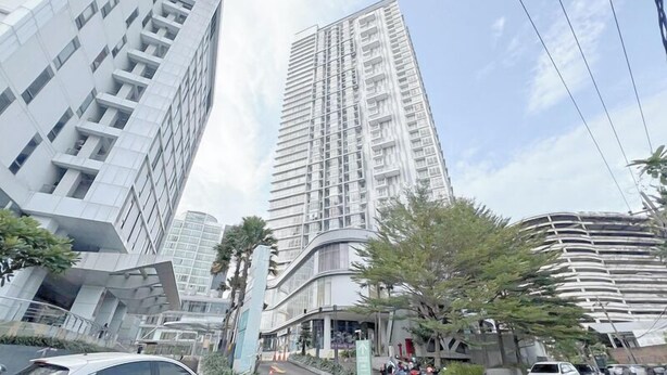 A modern high-rise building with a glass facade, surrounded by other contemporary buildings and palm trees. - 2Br Near Marvell City Mall At Linden Apartment (Surabaya)