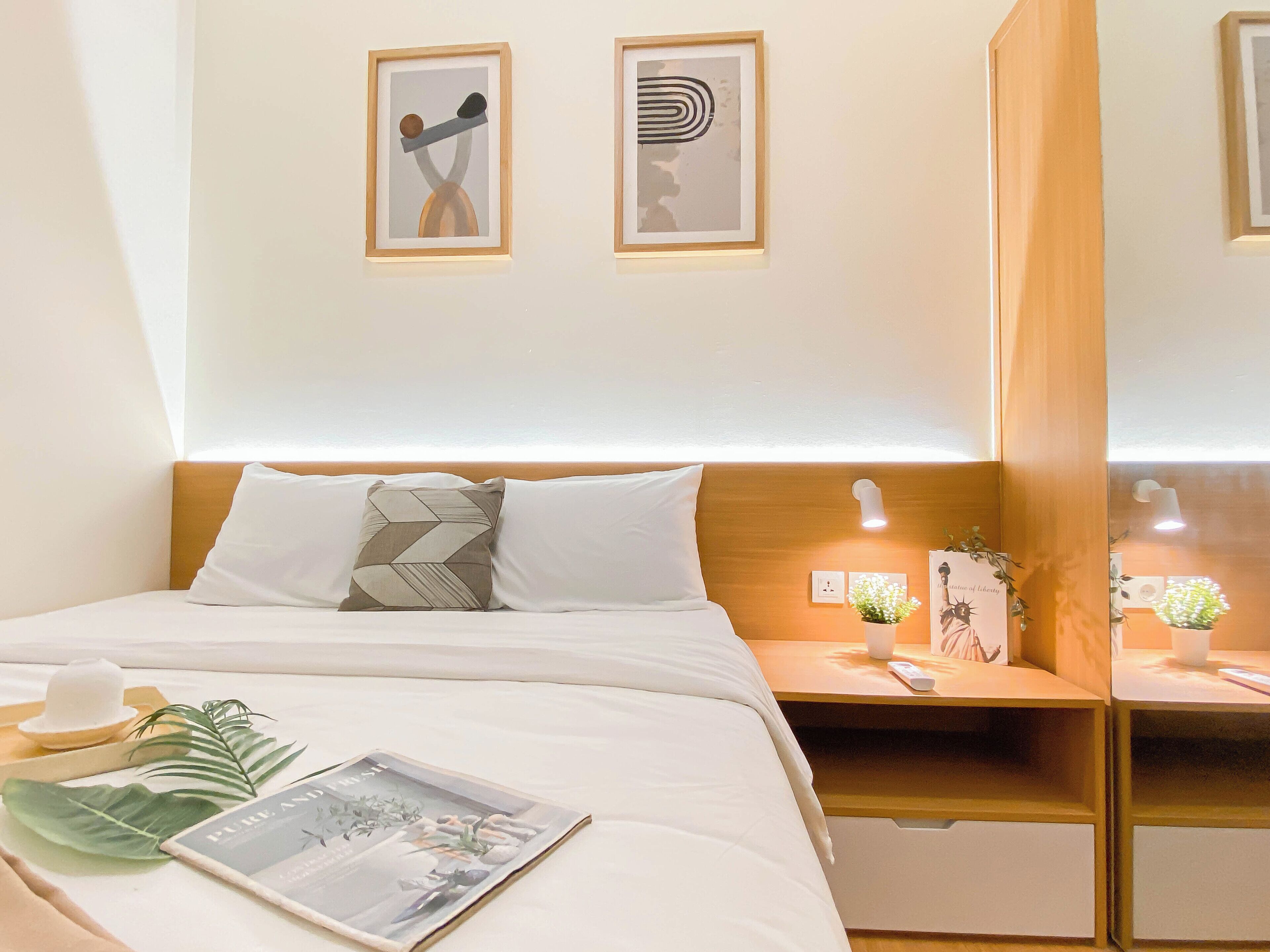 A neatly arranged hotel room with a bed, bedside tables, and two framed artworks on the wall.
