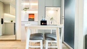 A modern kitchen with a white countertop, a black travel bag, and a painting of a sunset. - Modern Classic Touch 1Br Apartment At Tokyo Riverside Pik 2 (Teluknaga)
