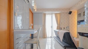 A hotel room with a bed, a desk, a chair, a large window with curtains, and a minibar. - 2Br Apartment Connected To Mall At Cinere Bellevue Suites (Depok)