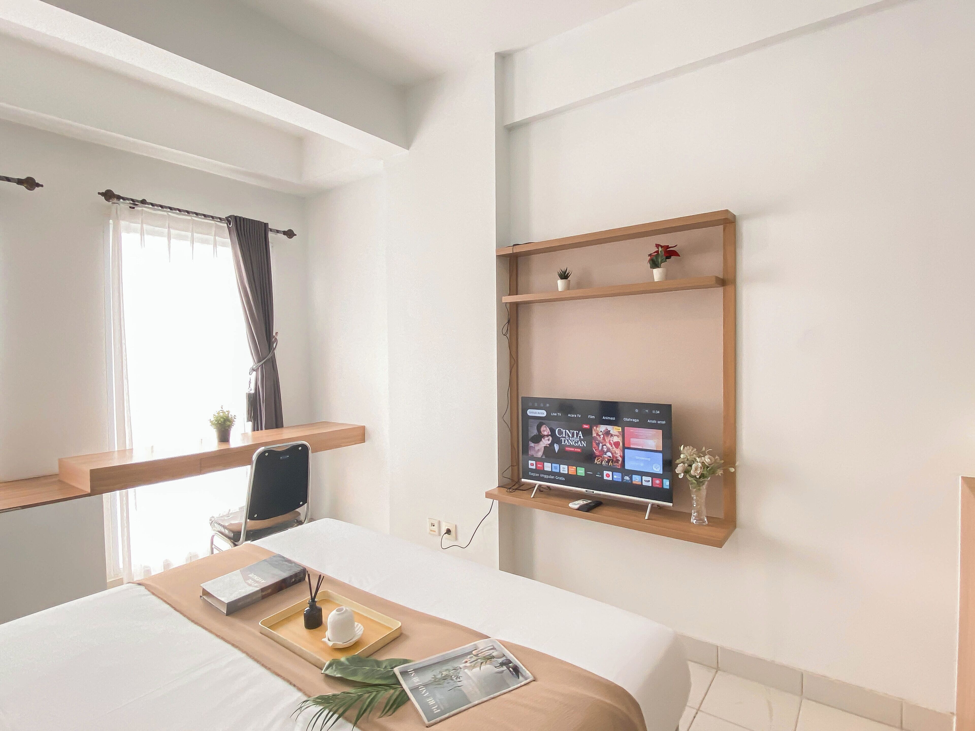 A modern hotel room with a bed, bedside table, TV, and a window with curtains.