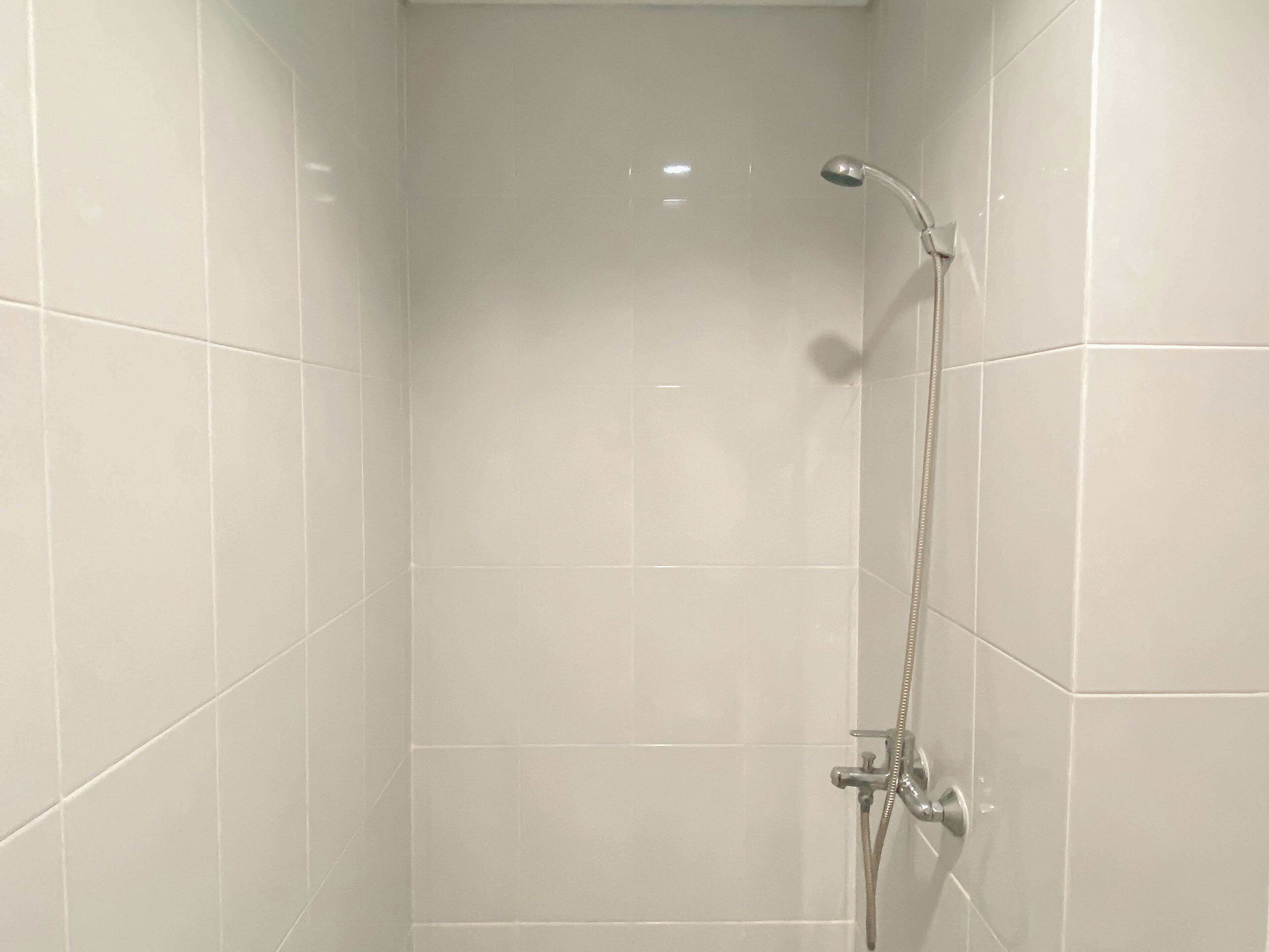 A bathroom with white tiled walls and a shower with a handheld showerhead.