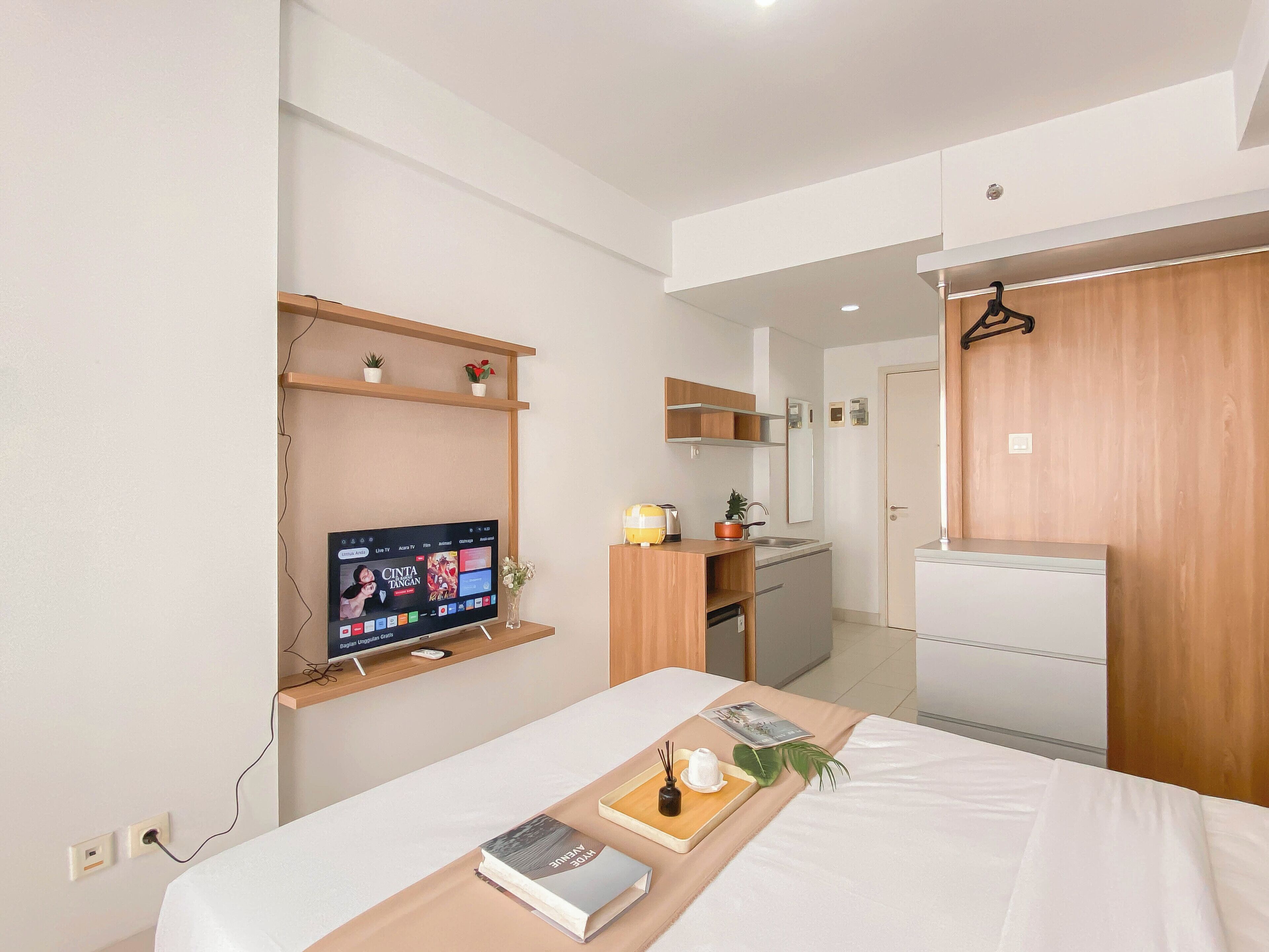 A modern hotel room with a bed, a TV, a small kitchenette, and a wooden wardrobe.