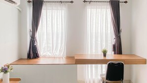 A room with a desk, chair, and two windows with curtains. - Standard Look Studio At Patraland Urbano Apartment (Bekasi)