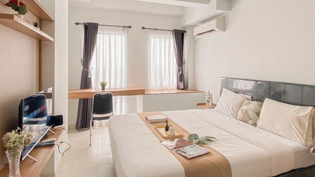 A hotel room with a bed, bedside table, desk with a computer, and a window with curtains. - Studio Near Bekasi Station At Patraland Urbano Apartment (Bekasi)
