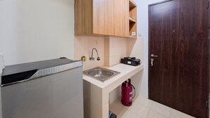 A compact kitchen with a refrigerator, sink, wooden cabinets, and a fire extinguisher.