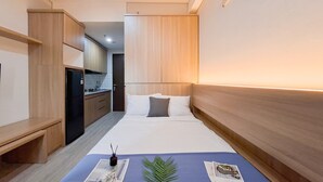 Een hotelkamer met een bed, nachtkastje, klein bureau en kitchenette.