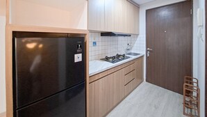 Een kleine keuken met een zwarte koelkast, houten kastjes, een wit aanrechtblad en een roestvrijstalen afzuigkap.