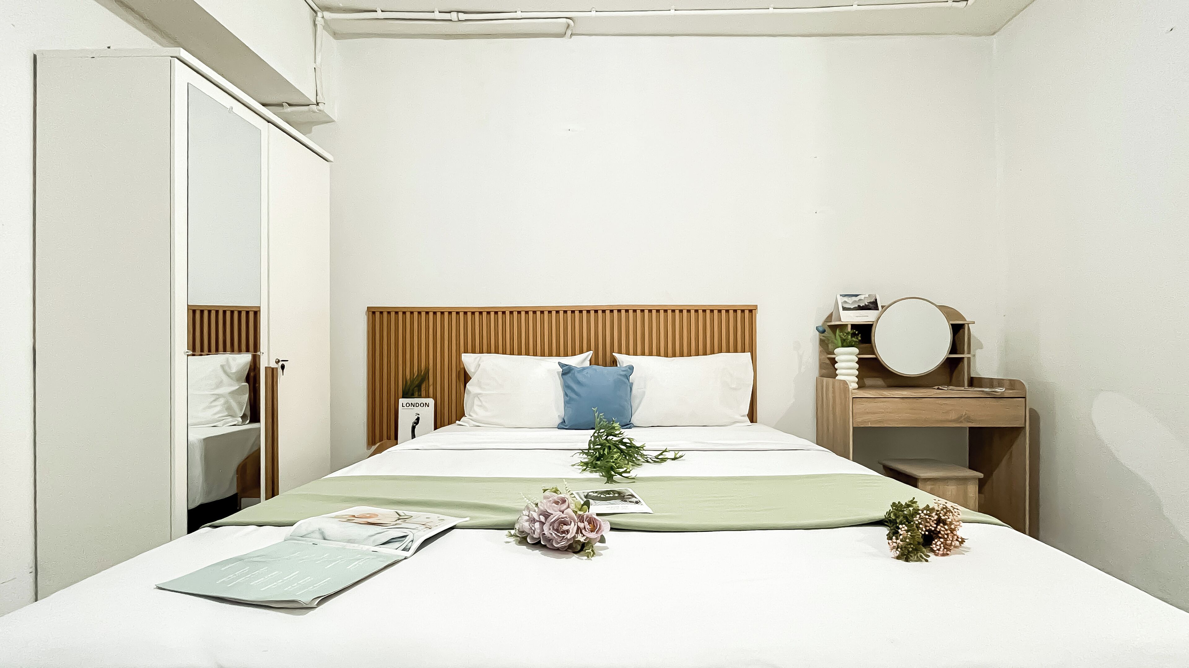 Hotellihuone, jossa on sänky, yöpöytä peilillä, toinen yöpöytä ja vaatekaappi.