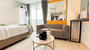 A modern hotel room with a bed, a sofa, a small table with a vase, and a mirror. - Modern And Tidy Studio Room At West Vista Apartment (Jakarta)