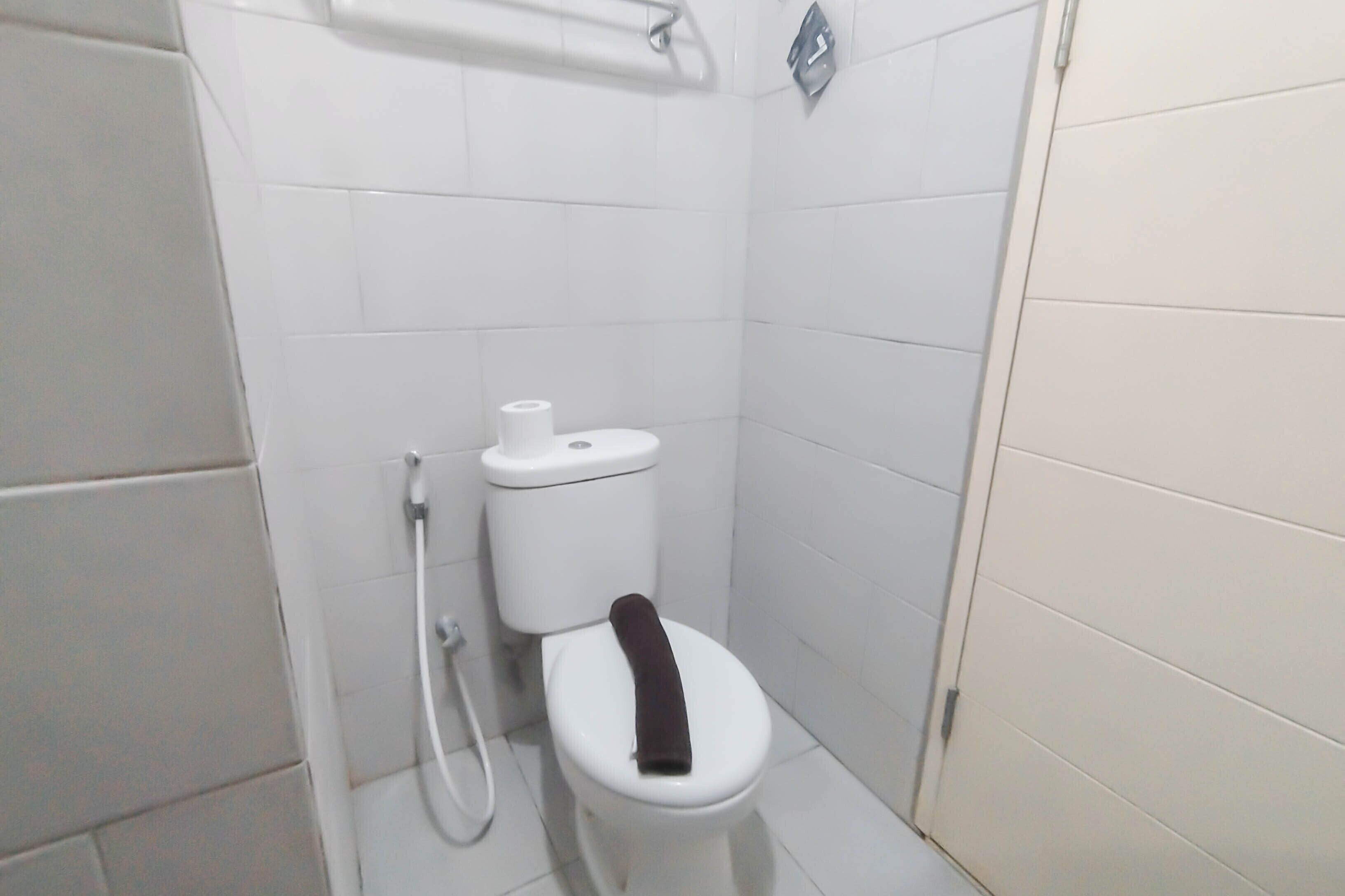A small, white bathroom with a toilet, a white towel hanging on the seat, and a white toilet paper holder on the wall.
