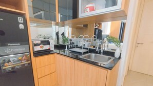 A modern kitchen with wooden cabinets, a black countertop, a sink, and a refrigerator. - Studio Near Mall (No Kitchen) At Benson Supermall Mansion Apartment (Surabaya)