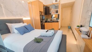 A modern hotel room with a large bed, a built-in desk, a small kitchenette, and a bathroom. - Studio Near Mall (No Kitchen) At Benson Supermall Mansion Apartment (Surabaya)