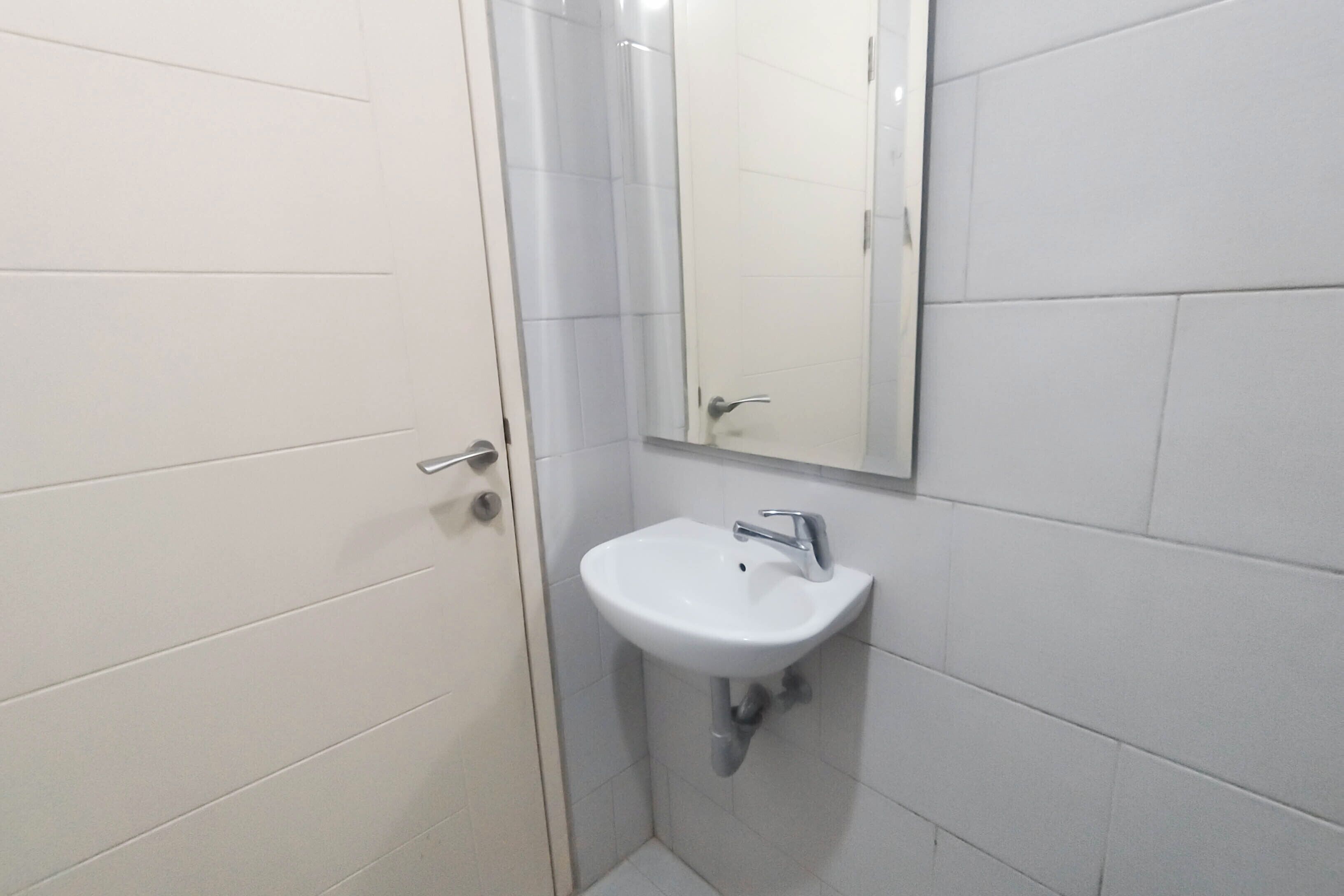 Een badkamer met witte tegels, een wastafel, een spiegel en een deur.