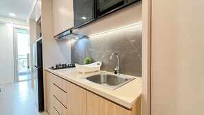 A modern kitchen with a stainless steel sink, a gas stove, and wooden cabinets. - Strategic Studio At Antasari Place Apartment (Jakarta)