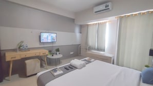A hotel room with a bed, a desk, a chair, a small table with a plant, and a TV on the wall. - Spacious And Modern Studio At Tanglin Supermall Mansion Apartment (Surabaya)