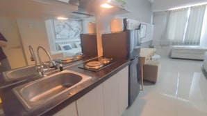 A modern kitchen with stainless steel appliances, a built-in oven, and a dining area with a white sofa and a small table. - Spacious And Modern Studio At Tanglin Supermall Mansion Apartment (Surabaya)