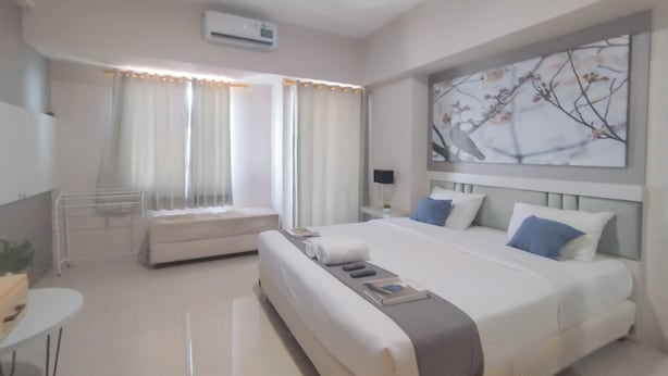 A modern hotel room with a large bed, a bedside table, a chair, and a window with curtains. - Spacious And Modern Studio At Tanglin Supermall Mansion Apartment (Surabaya)