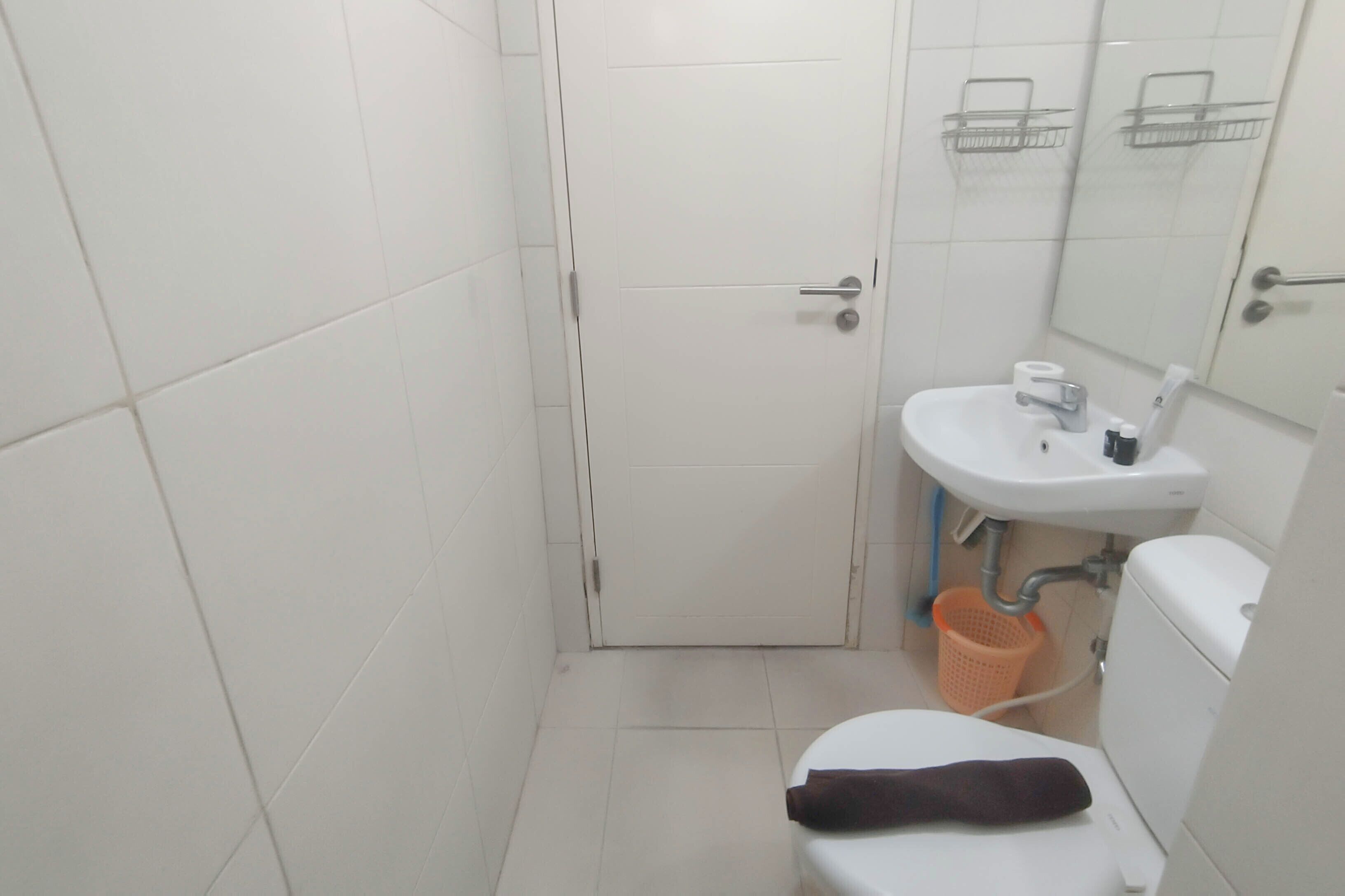 A small, clean bathroom with white tiles, a white sink, a toilet, and a door.