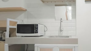 A kitchen with a microwave, sink, and wooden cabinets. - Small Studio (No Kitchen) Apartment At Bandaraya - Tallasa City Makassar (Makassar)