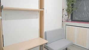 A small, compact room with a light grey bench, a wooden shelf, and a potted plant by the window. - Small Studio (No Kitchen) Apartment At Bandaraya - Tallasa City Makassar (Makassar)