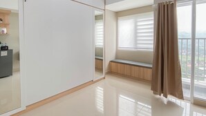 Quarto com guarda-roupa, um banco, janela com persianas e ar condicionado.