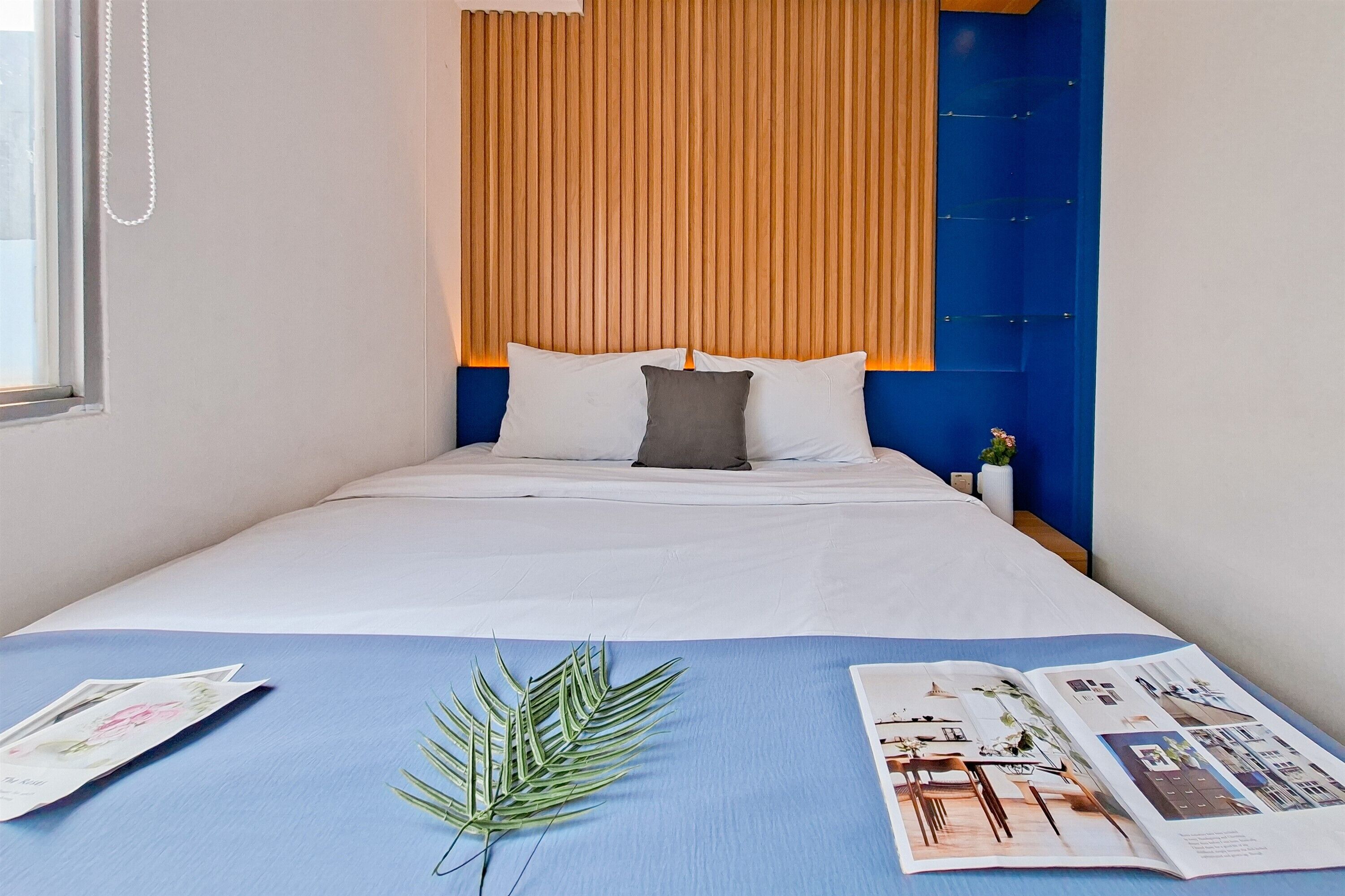Ein ordentlich bezogenes Bett mit weißen Laken, einer blauen Tagesdecke und einer Zeitschrift auf der Seite.