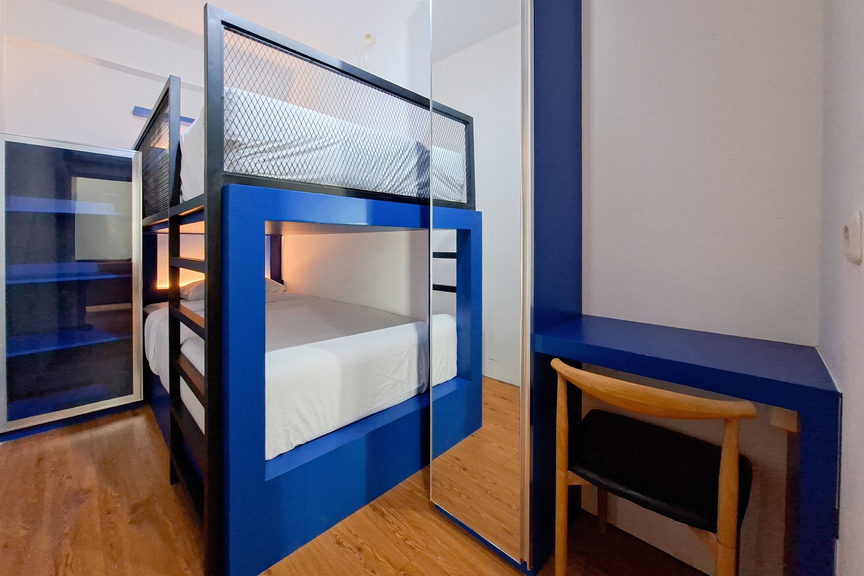A bunk bed with a mesh top, a wooden bench, and a mirrored wardrobe.
